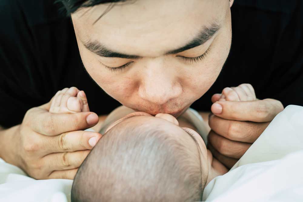 father kissing his newborn baby