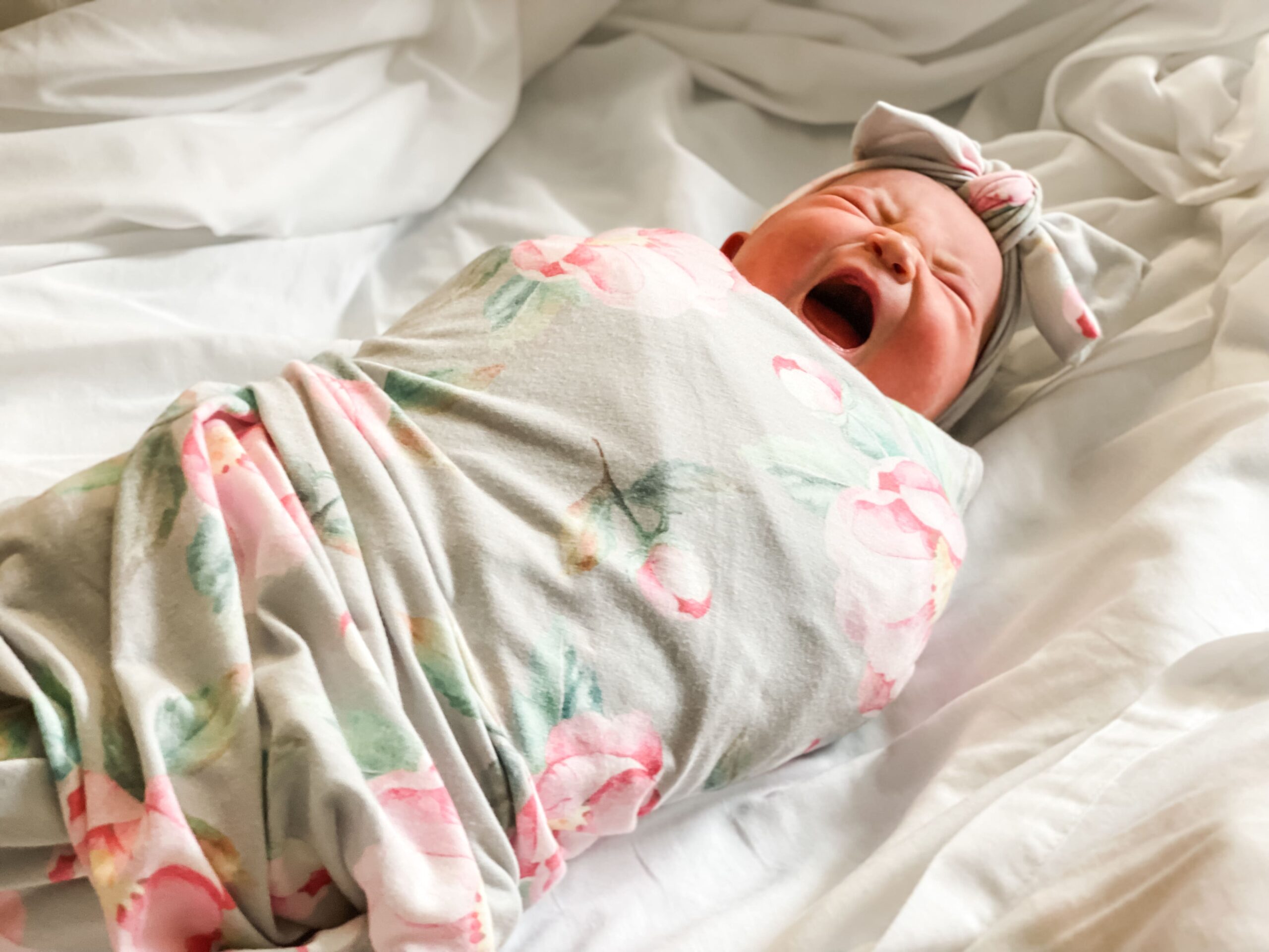 swaddled newborn baby yawning in bed